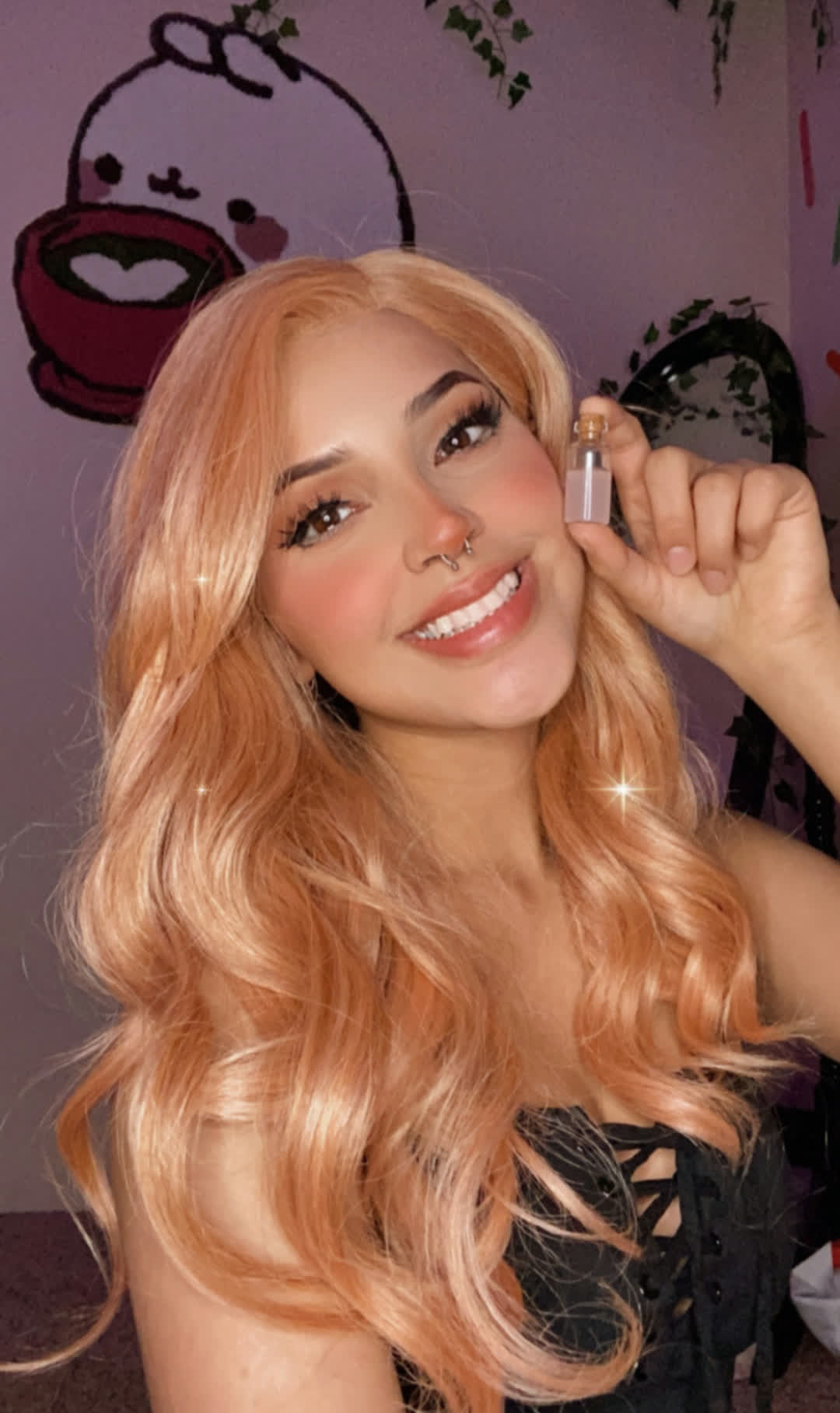 Close-up selfie in a black lace-up top against a purple cartoon mural with warm flash lighting.